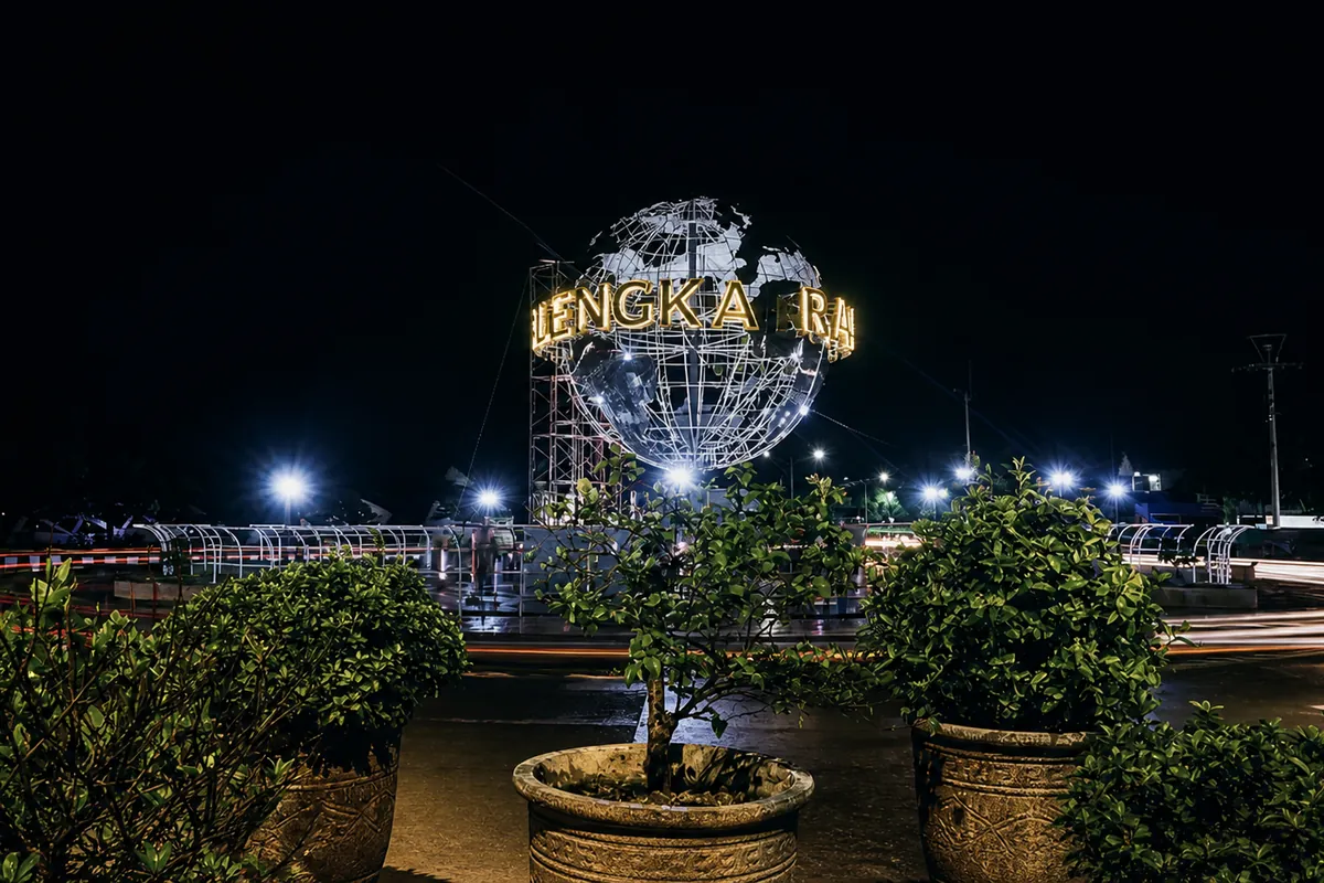 The illuminated steel globe monument at the Munjul roundabout at night, car light trails circling it.