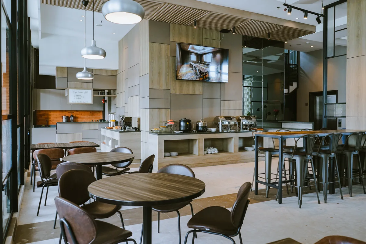 The Seruni breakfast room: a buffet counter with chafing dishes and an eggs station, round tables under pendant lights and a high communal table along the window.