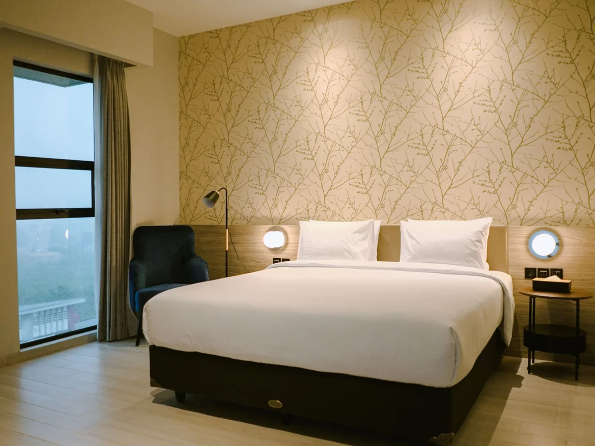 The Grand Suite: king bed against a patterned wall, armchair, and a window over the town.