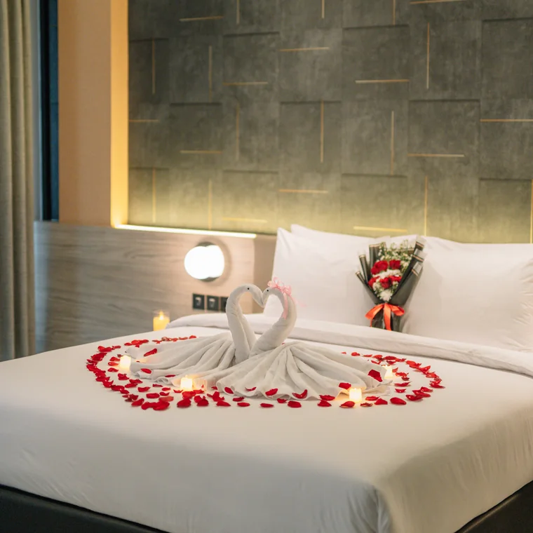 A suite dressed for a couple on their wedding night: towel swans and rose petals across the bed, candles lit, roses on the pillow.